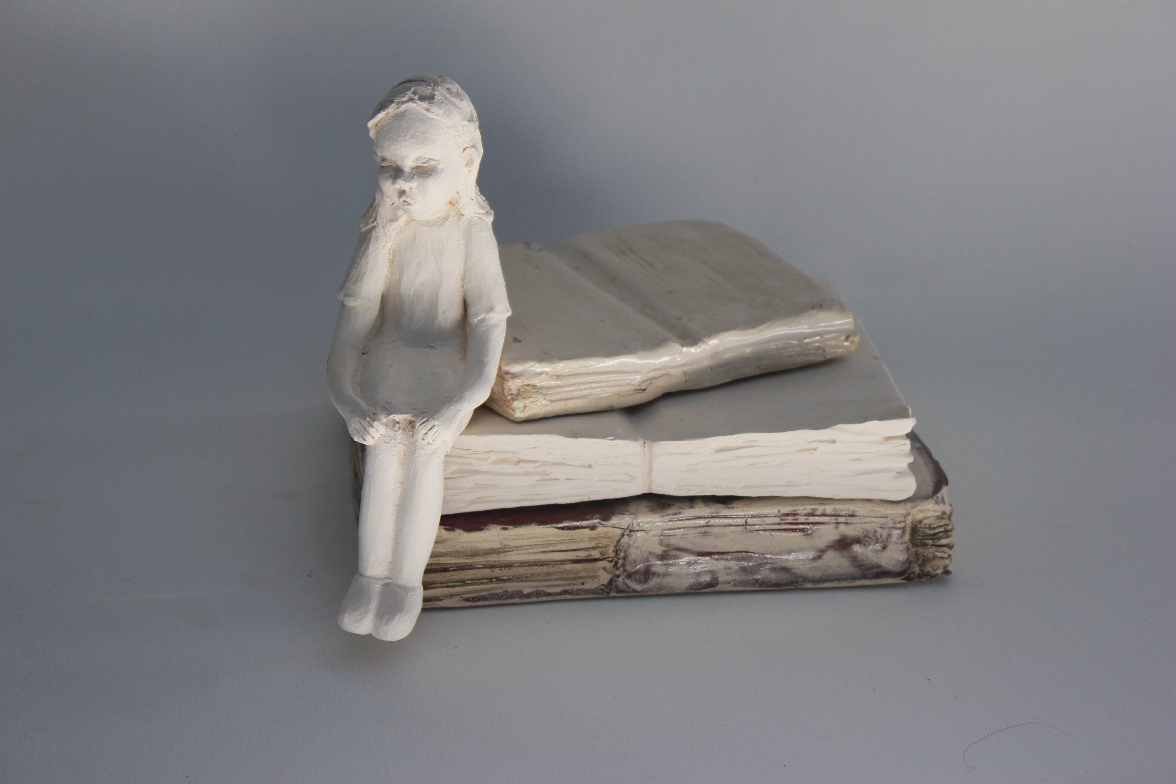 Niña de cerámica sentada sobre un libro