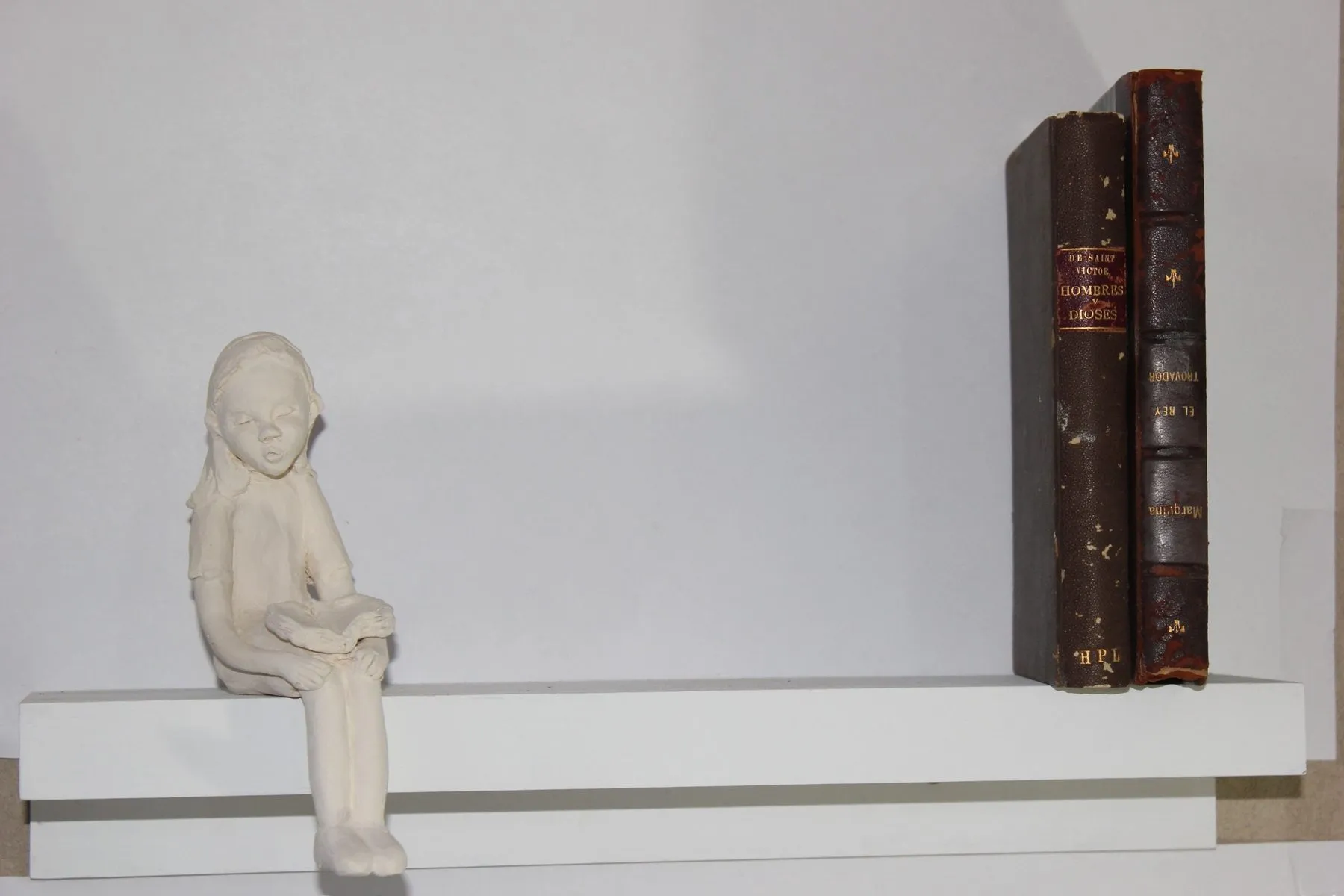 Ceramic girl sitting on a shelf next to two old books