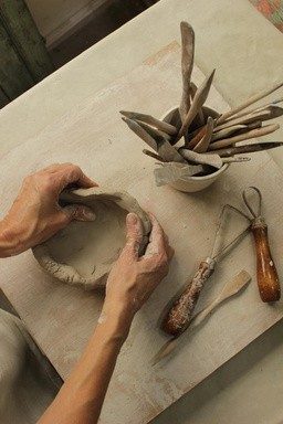 Manos trabajando la arcilla junto a herramientas de modelado