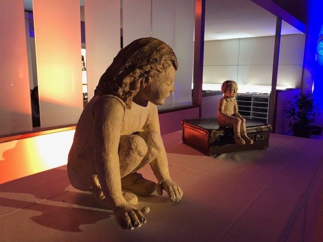 Mi niña interna: escultura de una niña en cuclillas, cerámica esmaltada, iluminada en sala