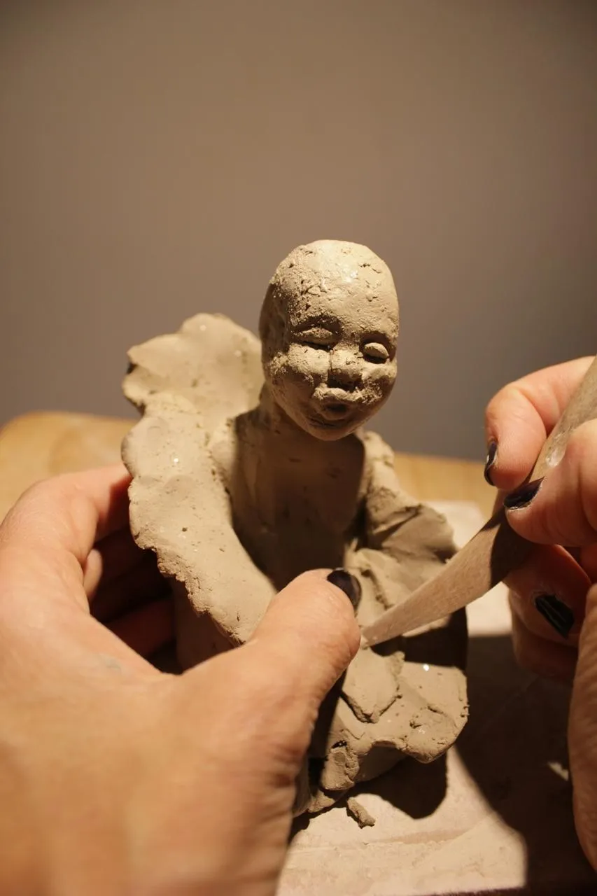 Detail of a clay figure in progress: a serene face held in the artist’s hands