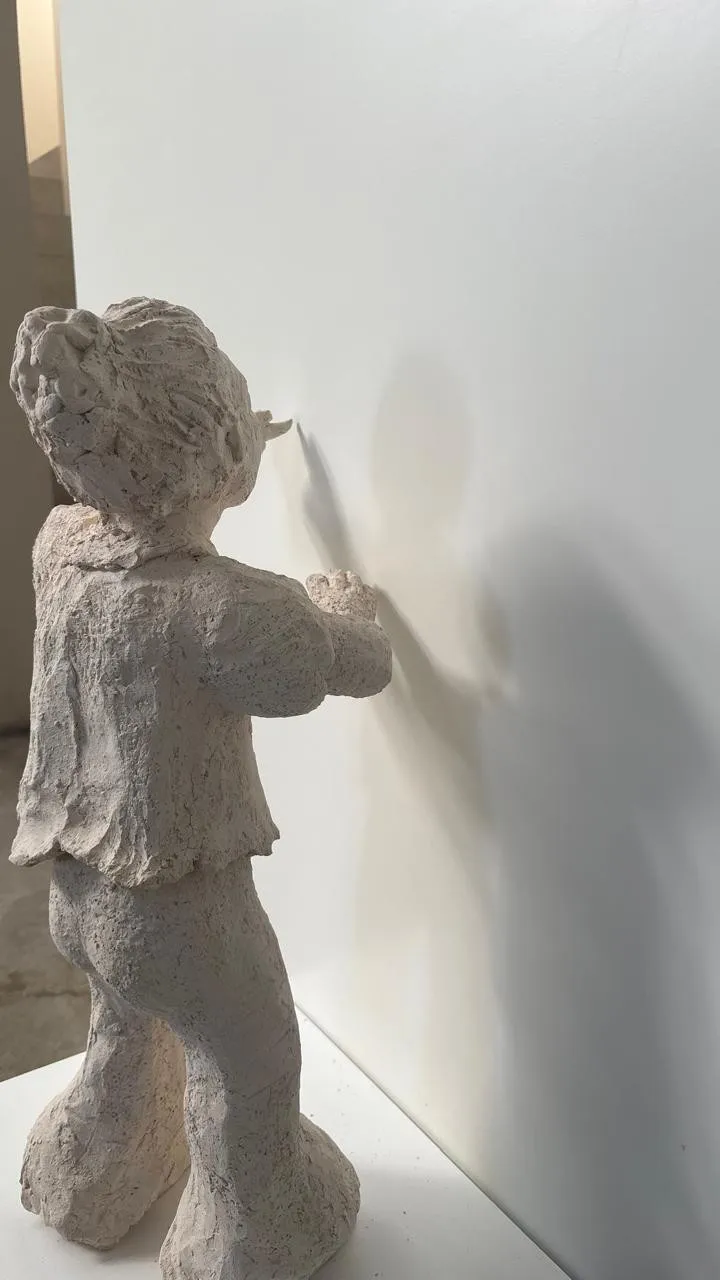 Tiempo circular: escultura de una niña de espaldas que escribe sobre la pared con el dedo, proyectando su sombra