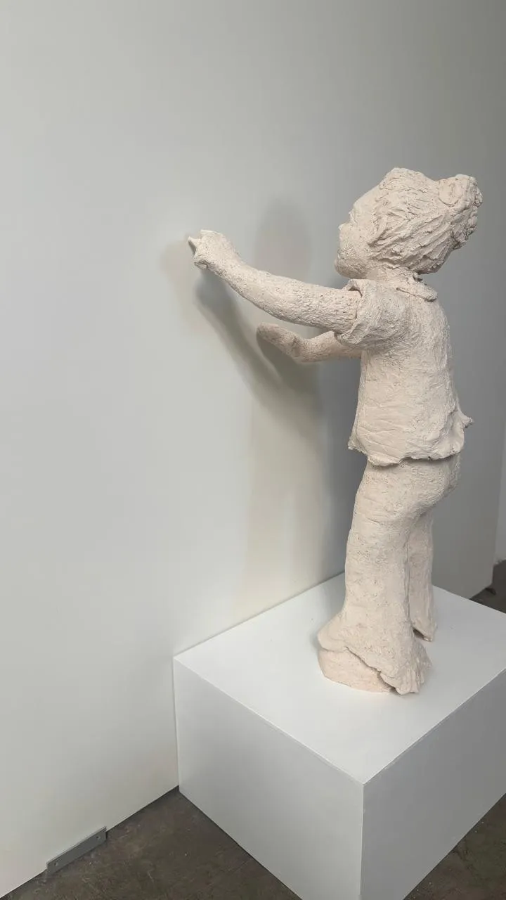 Vista lateral de la escultura, con los brazos extendidos hacia la pared