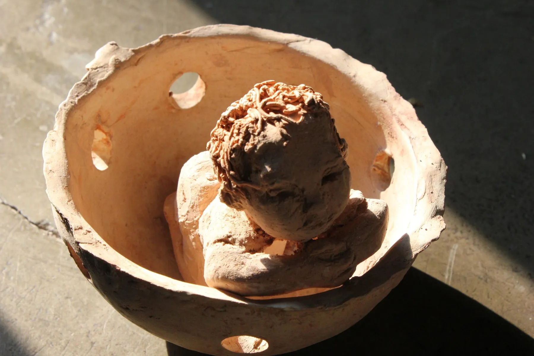 Head of a child modelled inside a pierced ceramic bowl