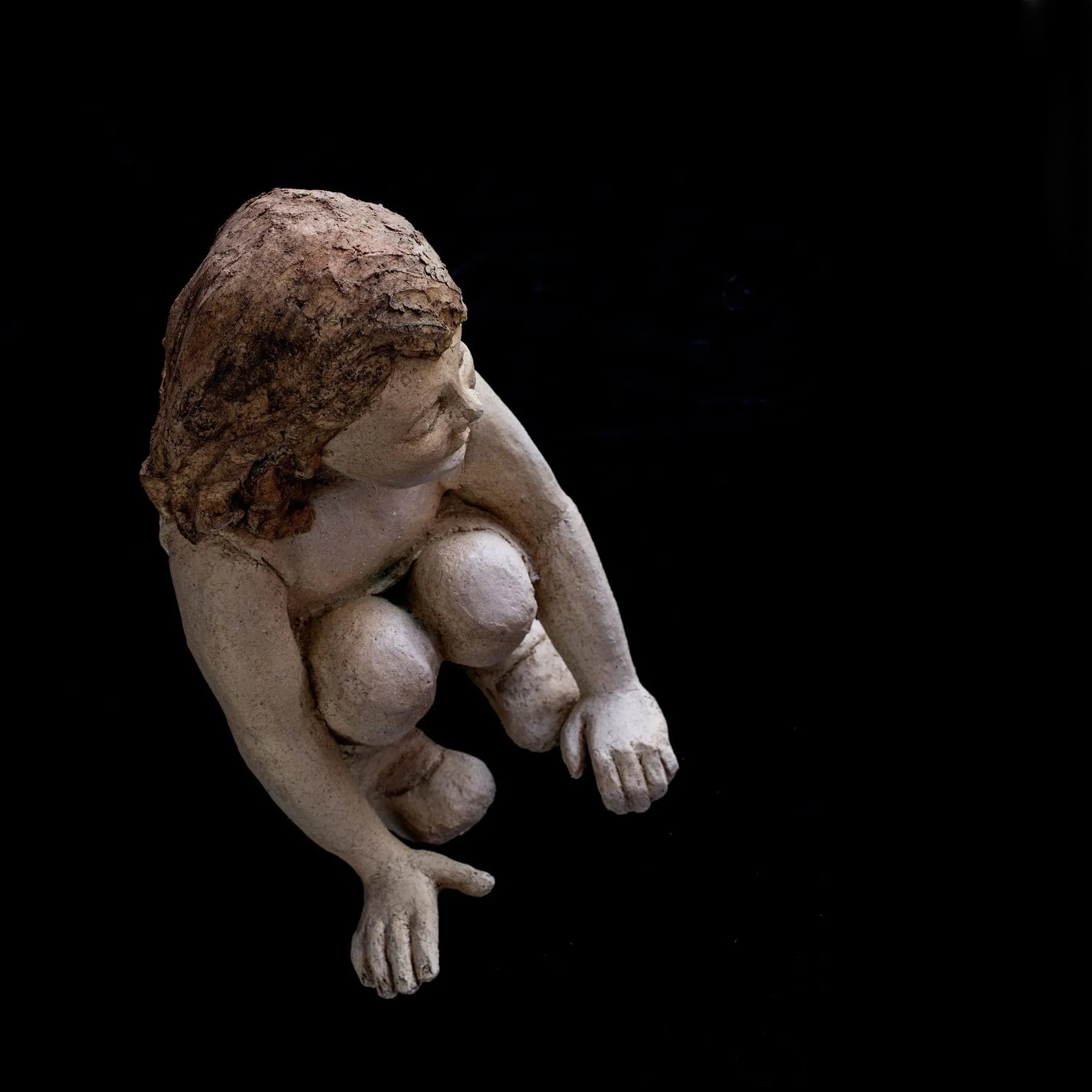 Figure of a crouching girl against a black background