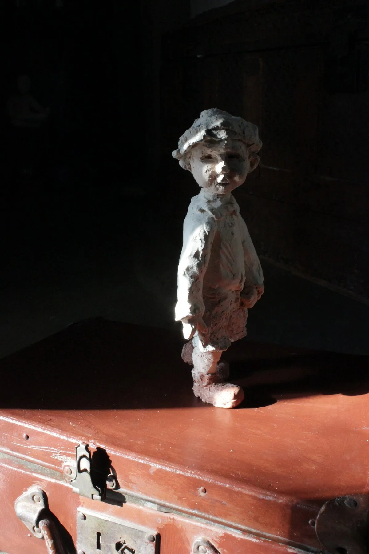 Figure of a boy in a cap standing on a trunk, lit from the side