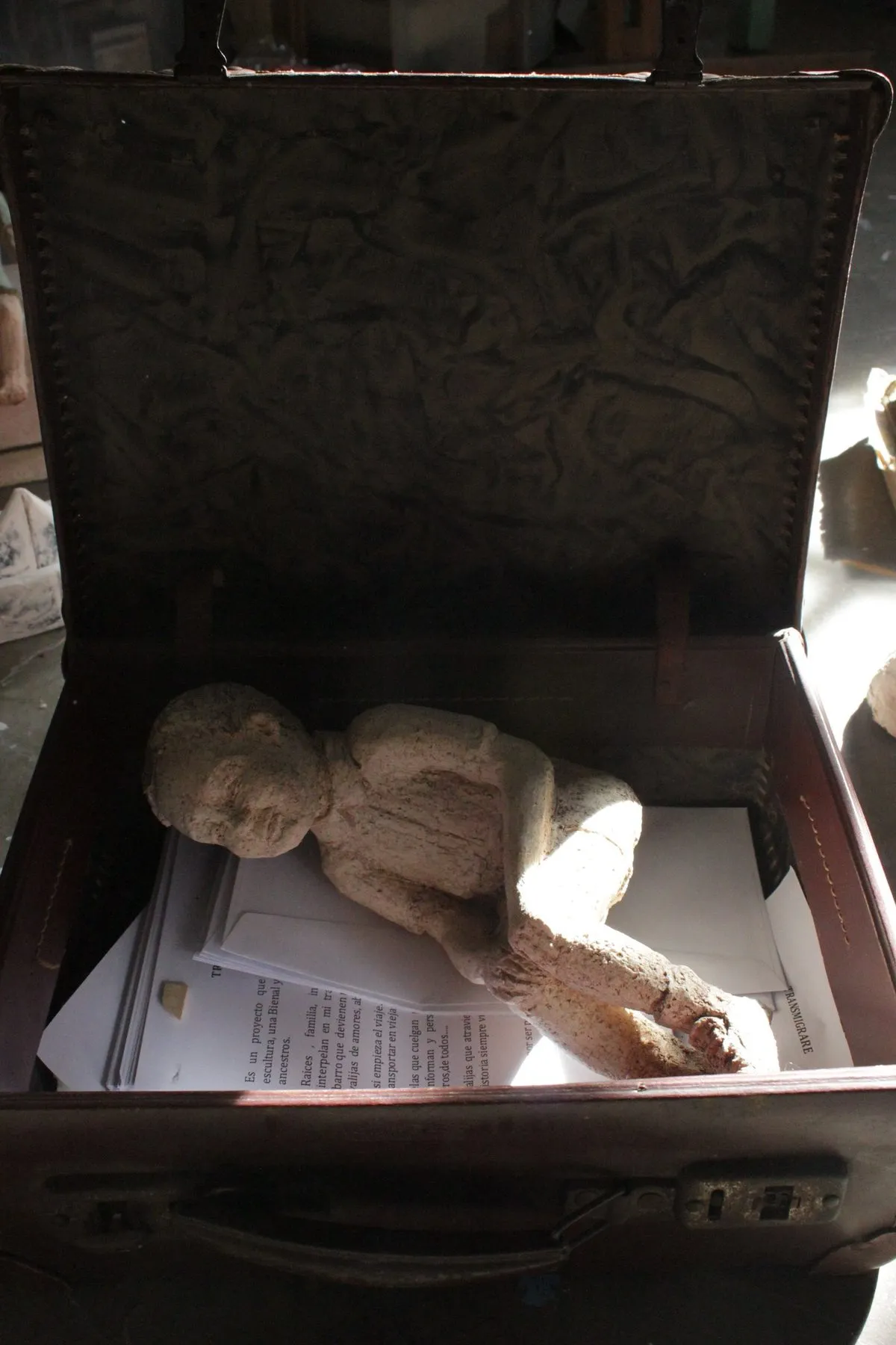 Figure of a boy lying inside an open suitcase full of papers
